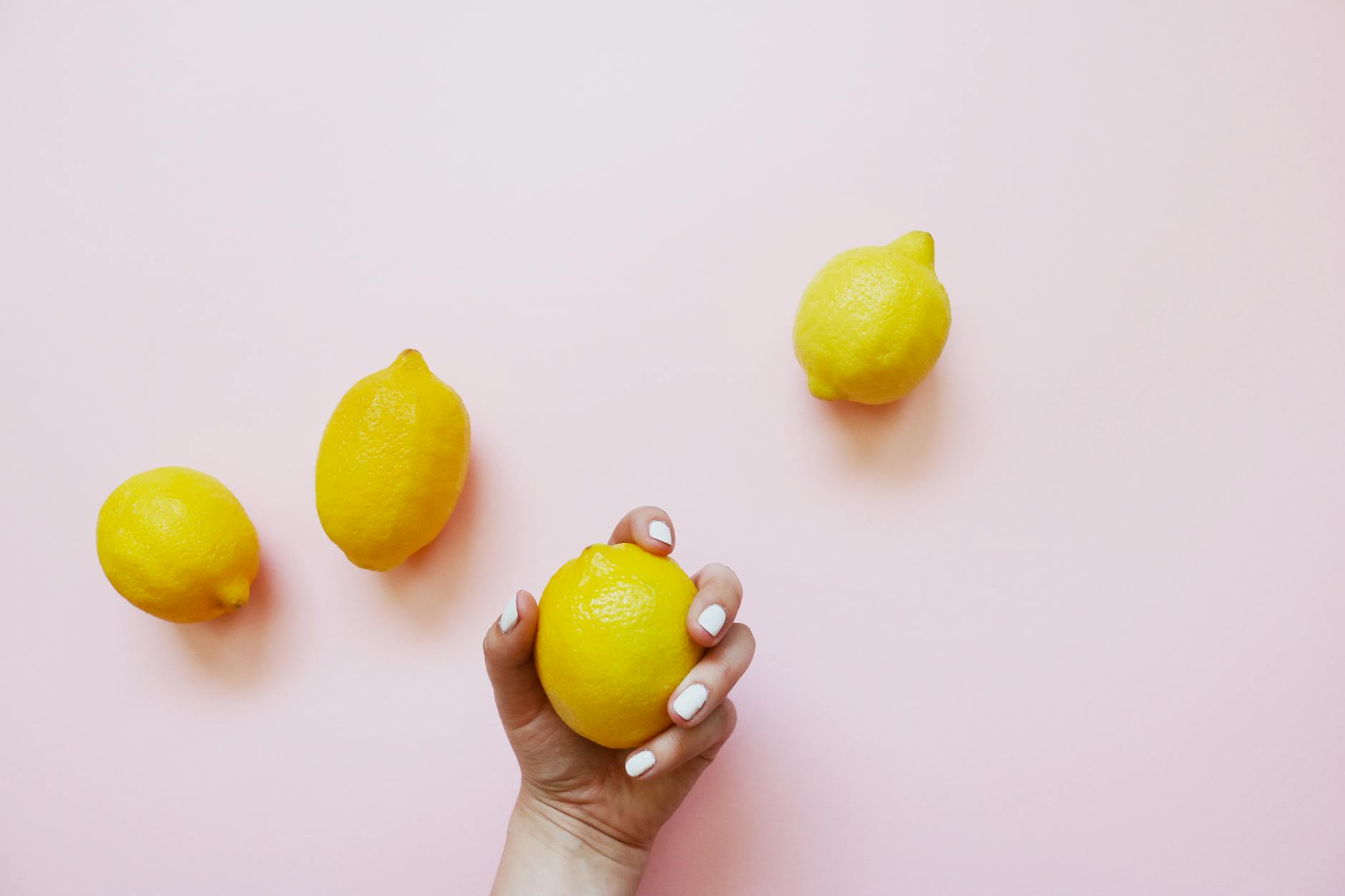 A hand holding fresh lemons on a soft pink background, symbolizing gentle reconnection and natural stimulation