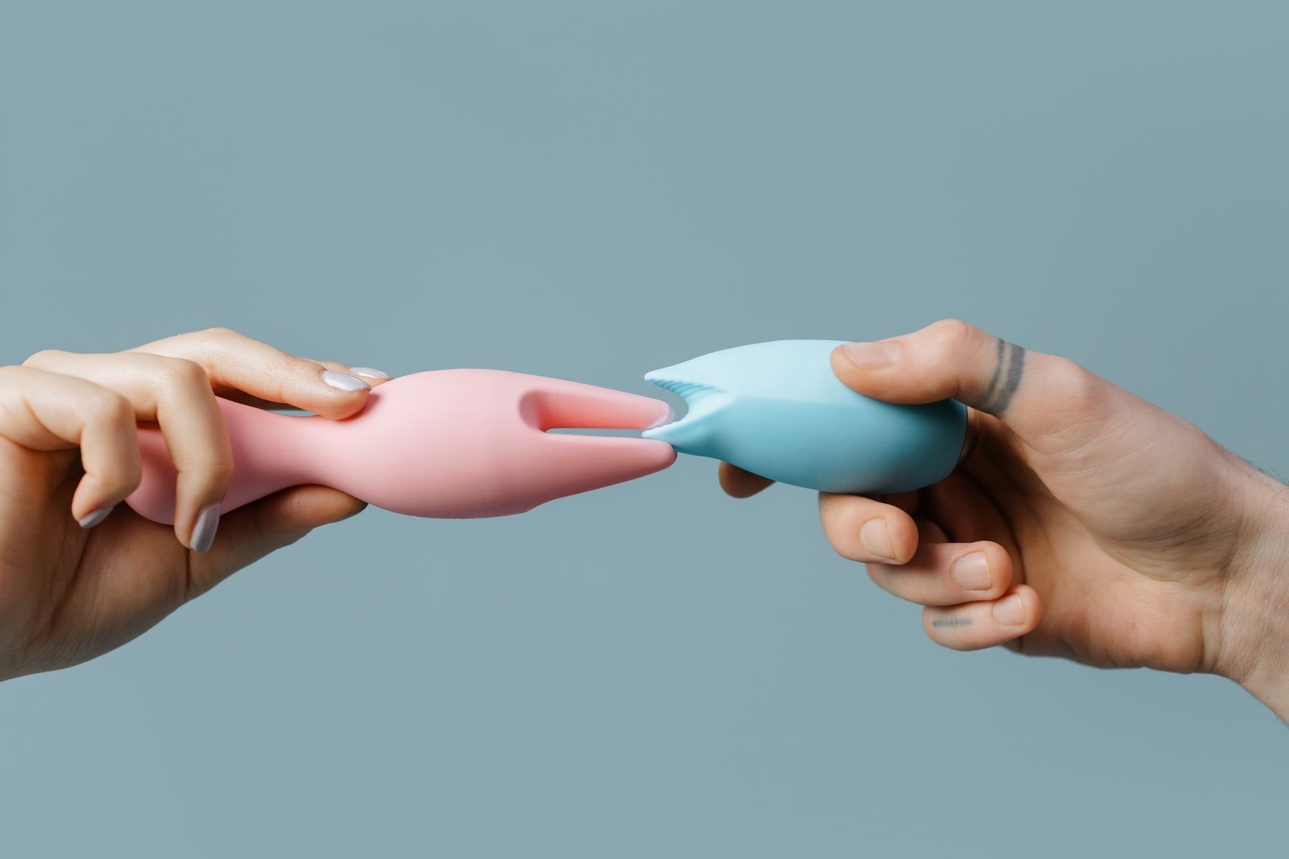 Hands holding pastel-colored silicone toys and vibrators on a soft background