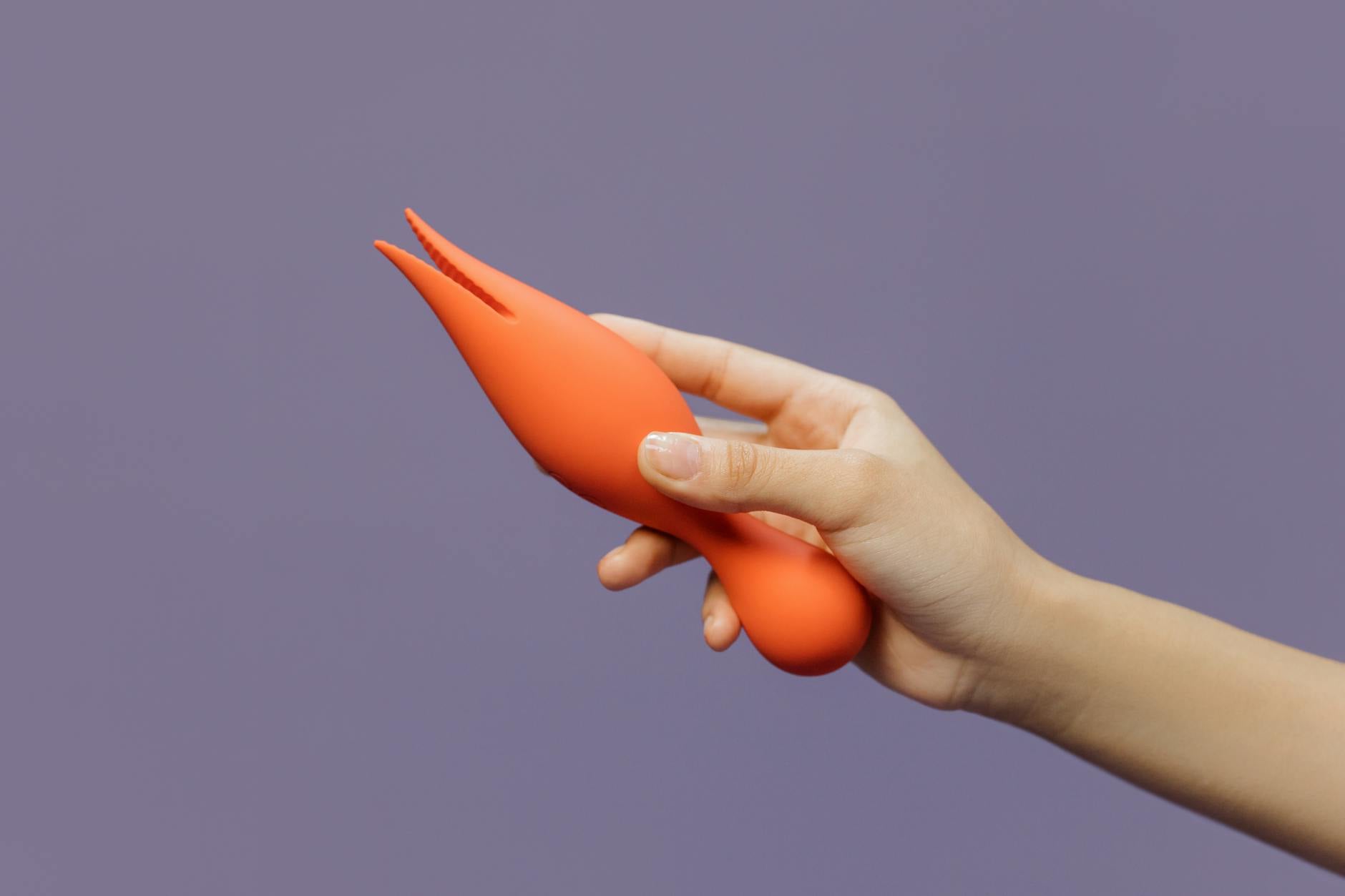 Close-up of a hand holding an orange vibrator against a minimalistic purple backdrop, symbolizing reclaiming sensation after surgery