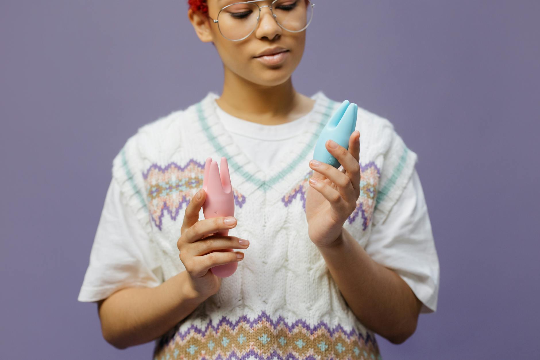 Woman with eyeglasses holding blue and pink silicone vibrators thoughtfully