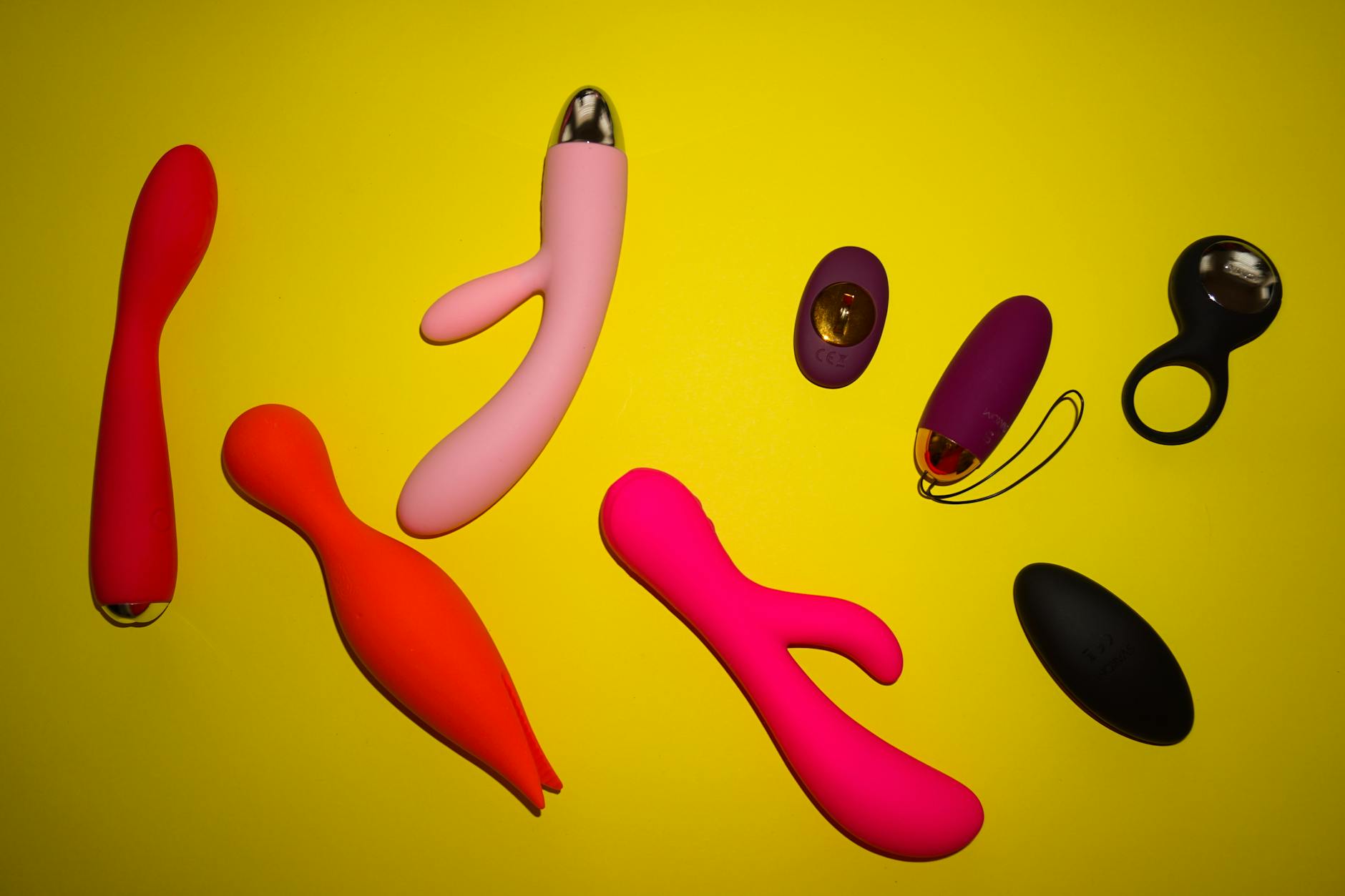 Vibrant collection of colorful sex toys arranged on a bright yellow surface, showcasing diversity in design